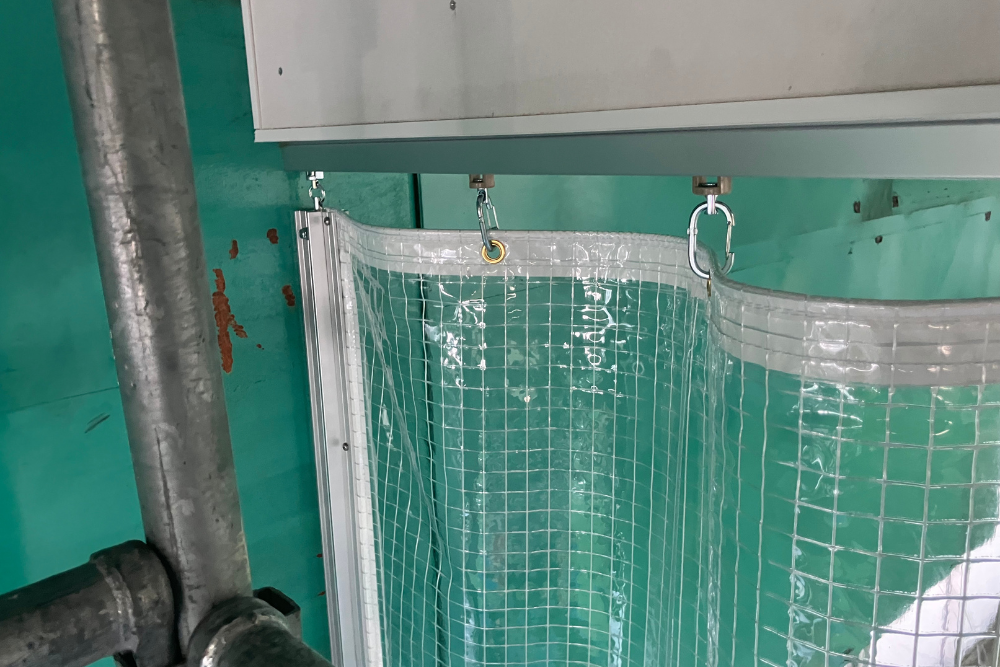 糸入り透明ビニールカーテンをカラビナでレールに吊り下げた取り付け部。