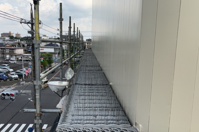 建物の外壁沿いに設置された足場通路。鳥の着地を防ぐための防鳥ピンが通路一面に隙間なく敷き詰められており、都市部での効果的な鳥害対策の様子を示しています。