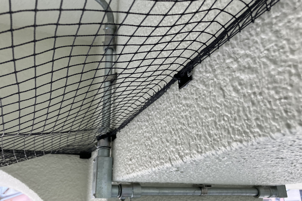 建物の梁や配管周りに沿って、隙間ができないよう精密に固定された防鳥ネットのクローズアップ