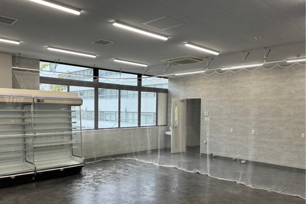 曲線を描く天井のレールに沿って店舗内の空間を区切るように張られた、開閉可能な白い防犯ネットの設置風景。