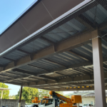 高所作業車を用いた大型施設の庇下への施工風景。広範囲の天井部分全体に鳥よけネットを綺麗に展張している様子