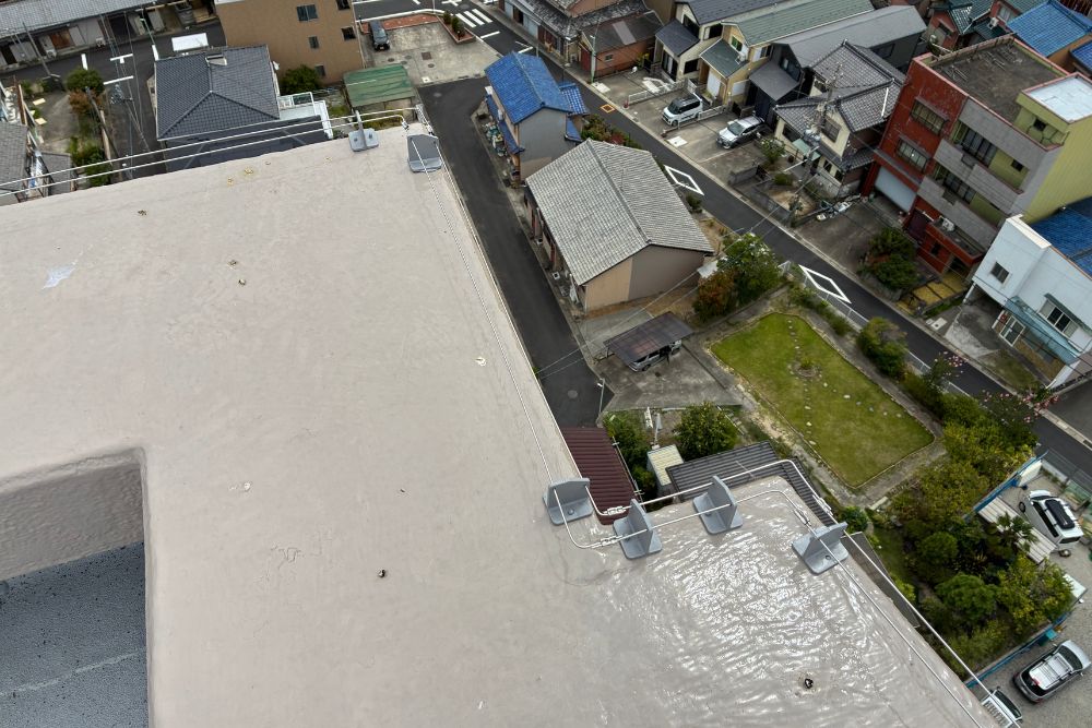 建物の屋上パラペット部分に沿って設置された、鳥害対策用の微弱電流ワイヤーの施工事例。眼下には住宅街の風景が広がっています。