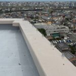 市街地と川を見渡すビル屋上の外周全体に張り巡らされた、防鳥ワイヤーの設置風景。景観を損なわずに広範囲の鳥害を防ぐ施工例です。