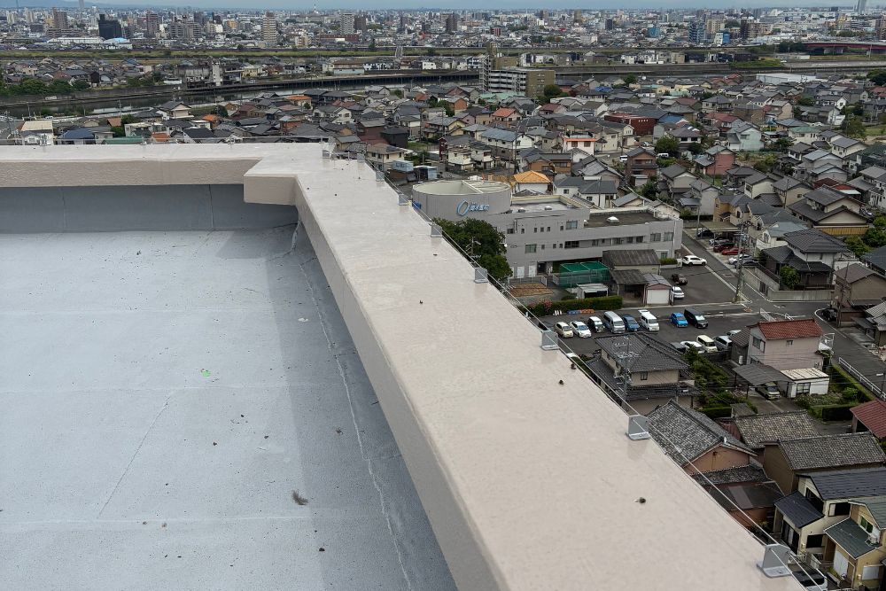 市街地と川を見渡すビル屋上の外周全体に張り巡らされた、防鳥ワイヤーの設置風景。景観を損なわずに広範囲の鳥害を防ぐ施工例です。