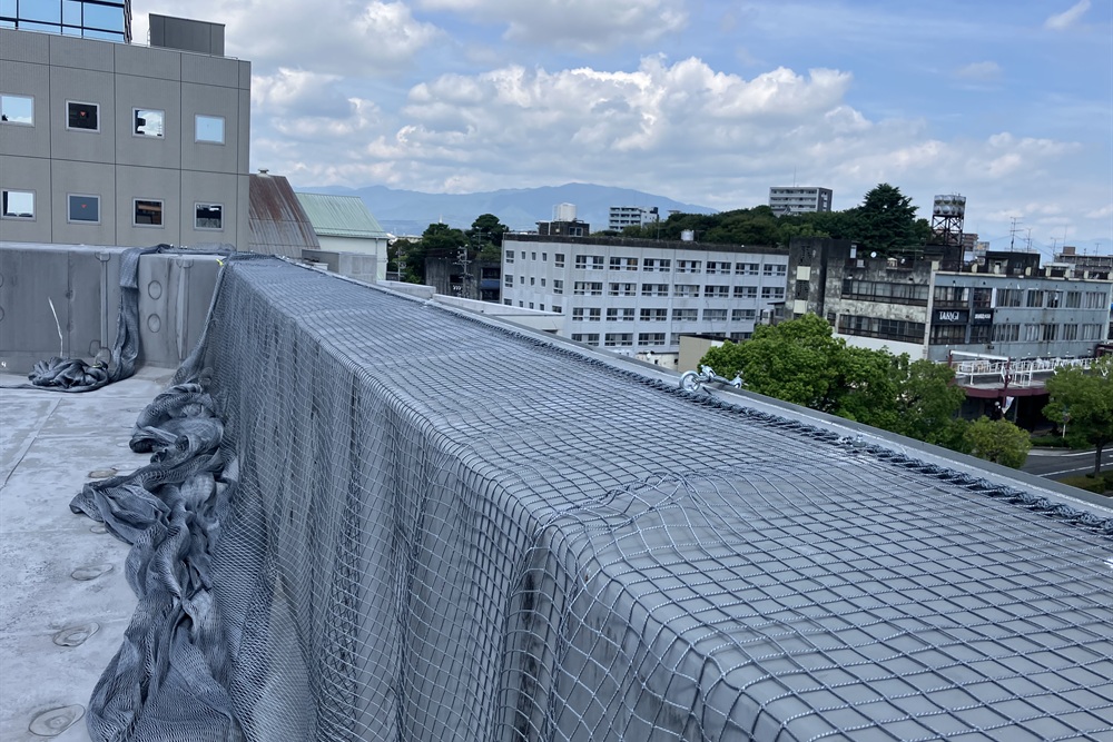 ビル屋上のパラペットに外壁剥落防護ネットを施工している様子。