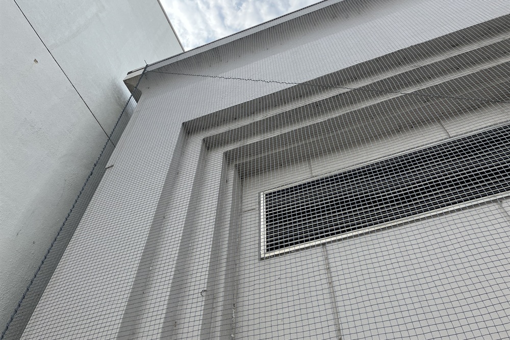 外壁の換気ガラリ周りに外壁剥落防護ネットを設置した施工例。劣化した外壁材の落下から歩行者を守る安全対策